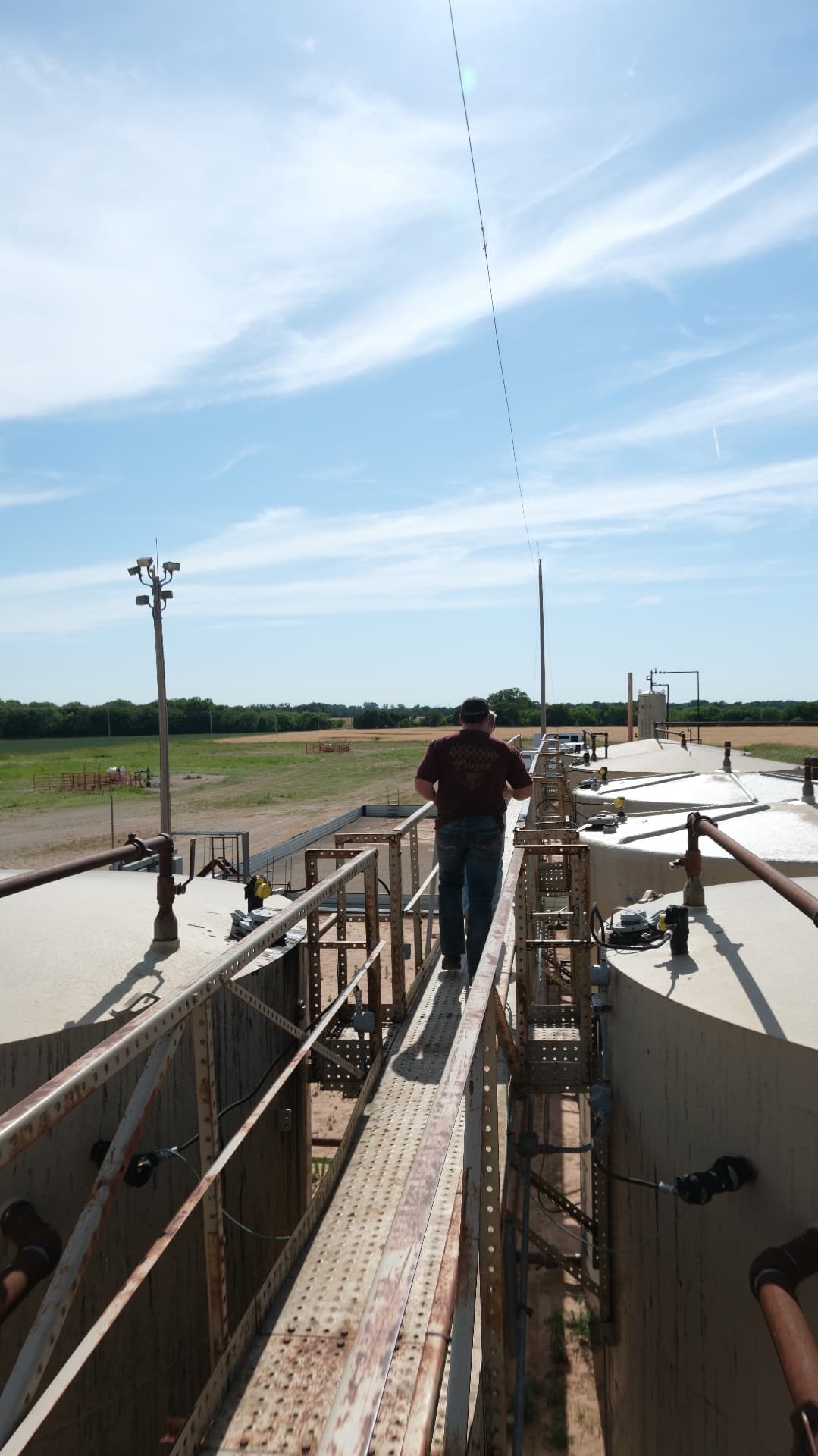 Operator walking a tank battery catwalk with monitoring hardware installed